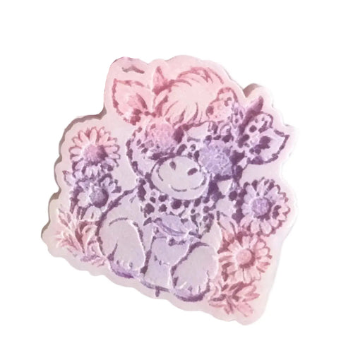 A pastel pink and purple wax melt featuring a cute cartoon highland cow surrounded by flowers, shown on a plain white background. wax melts