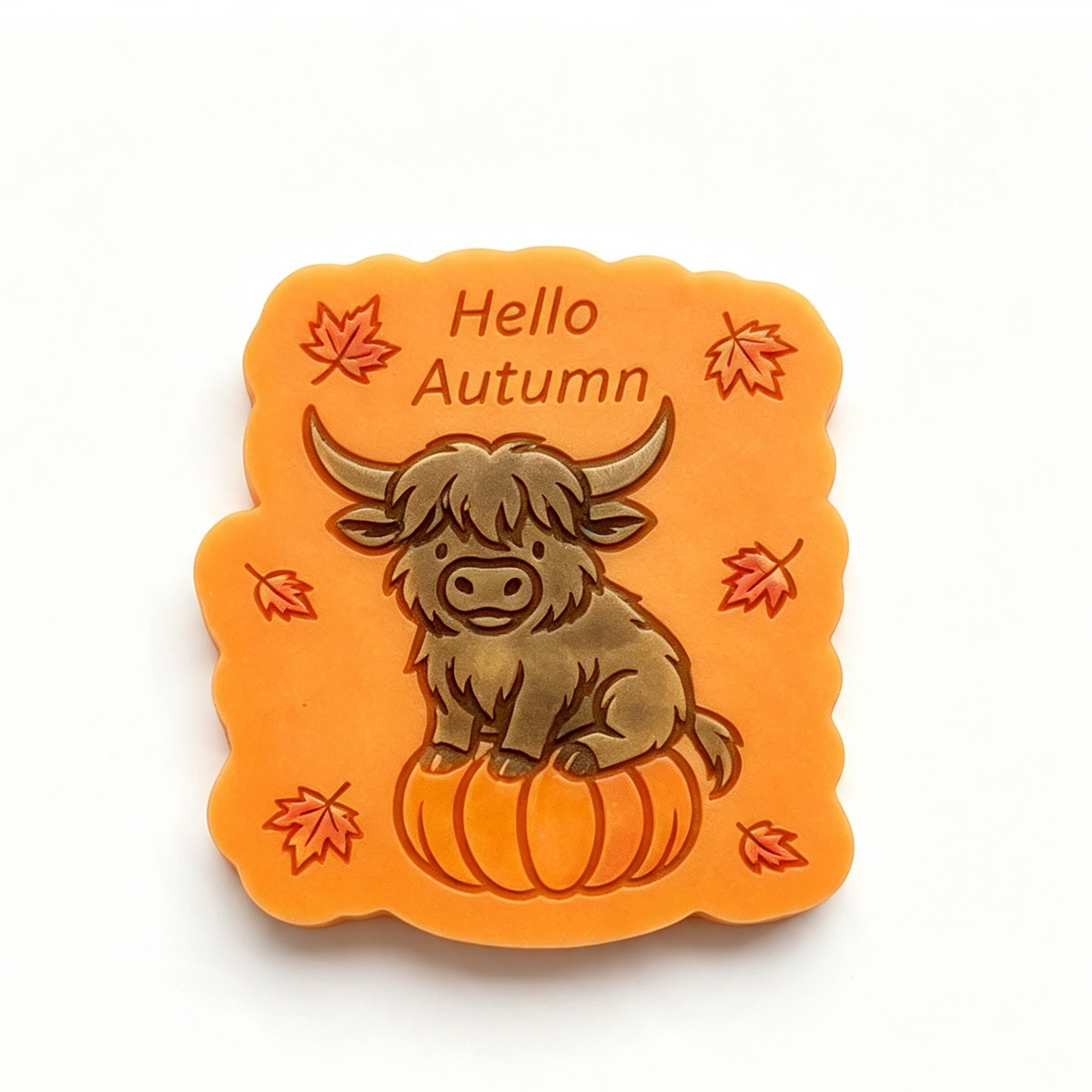 An orange scalloped square wax melt or plaque featuring a cartoon Highland cow sitting on a pumpkin with the words 'Hello Autumn' and small red autumn leaves, shown on a plain white background.