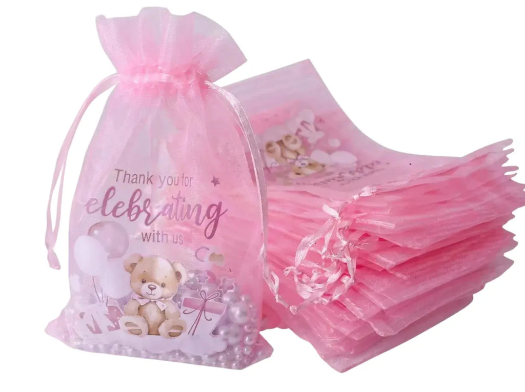 Pink tulle drawstring favor bags with teddy bear and balloon prints, shown with one filled bag and a stack of empty bags on a white background.