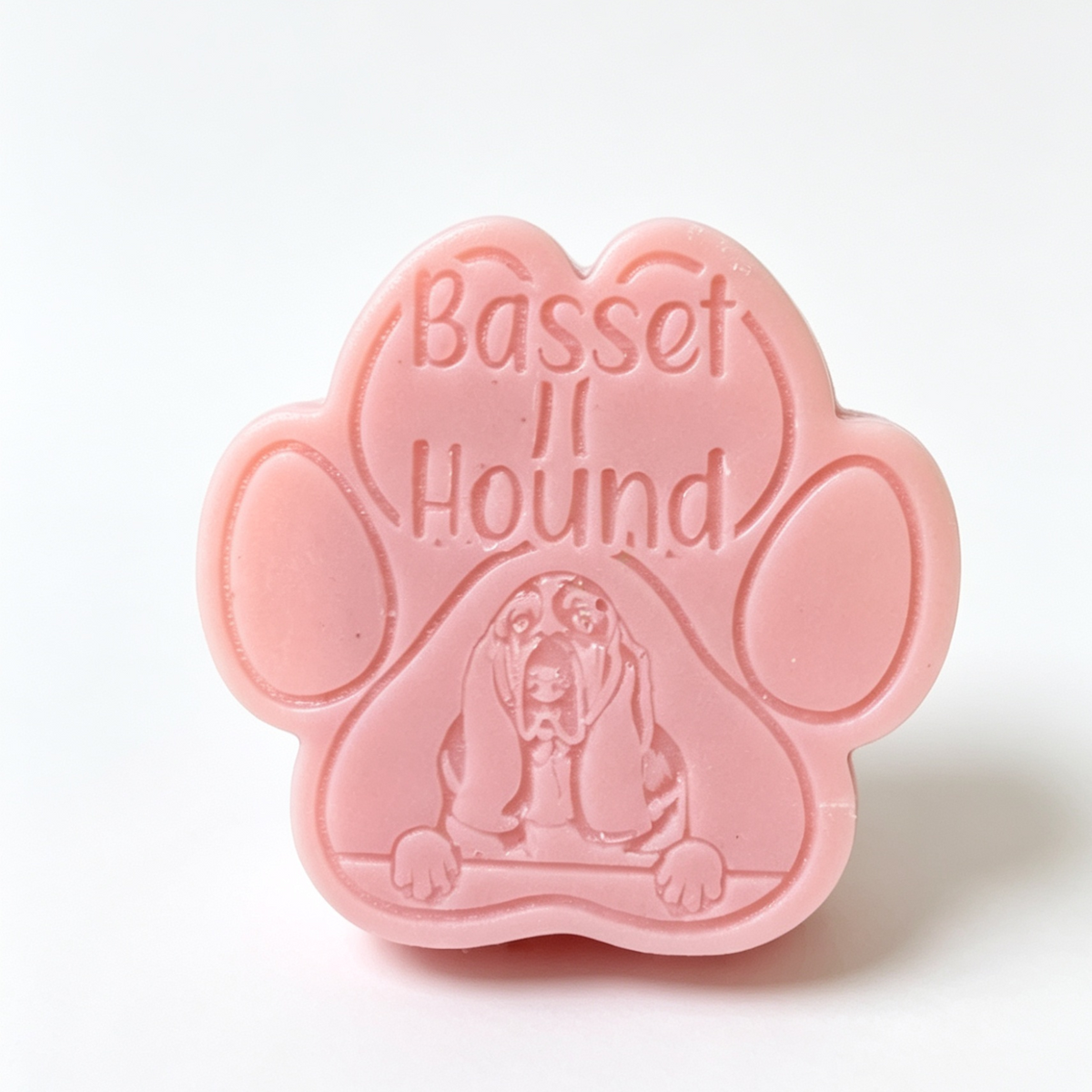 A pink paw-shaped wax melt embossed with the words 'Basset Hound' and an illustration of a basset hound, shown on a clean white background.