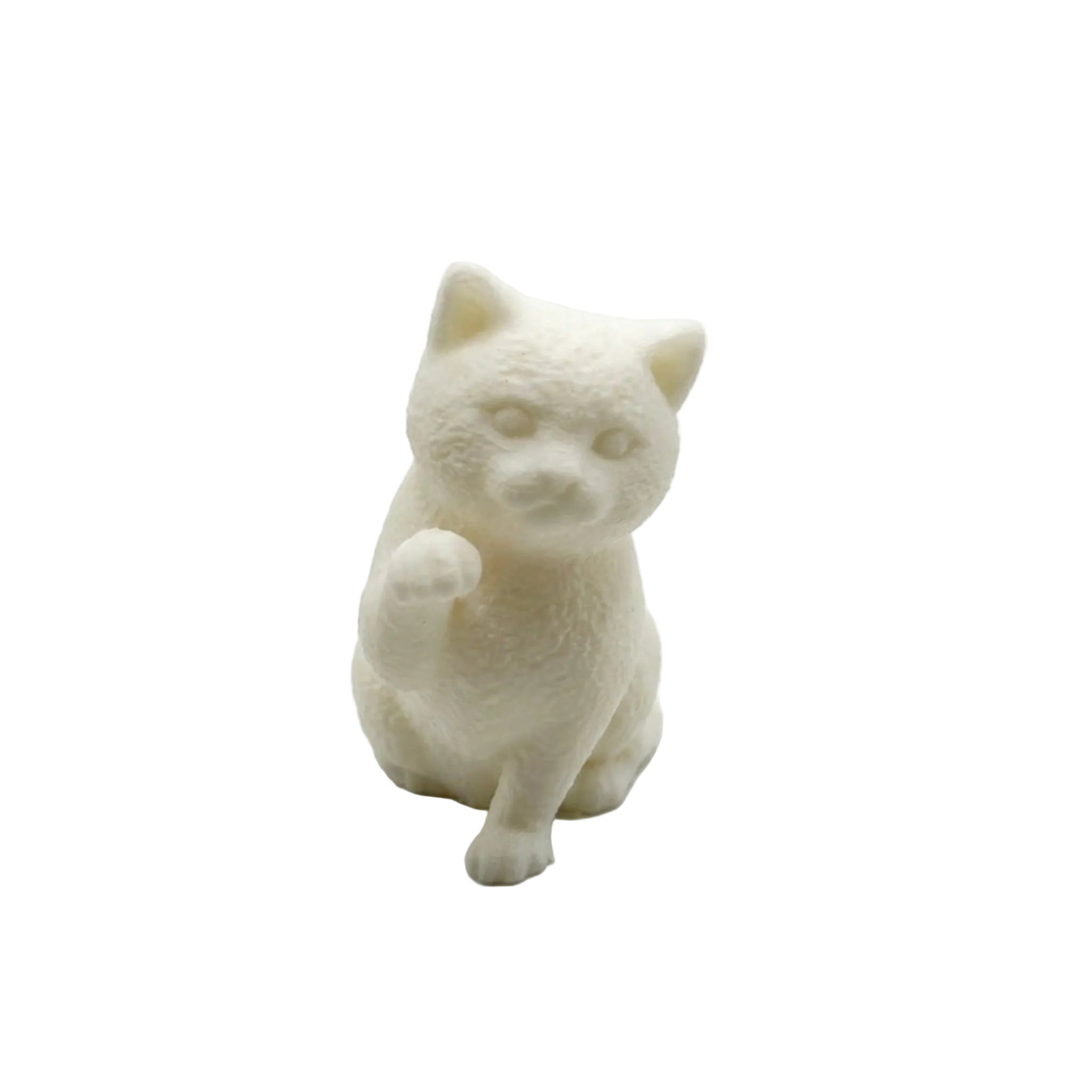 A small white cat figurine sitting upright with one paw raised, photographed against a plain light gray studio background. candle