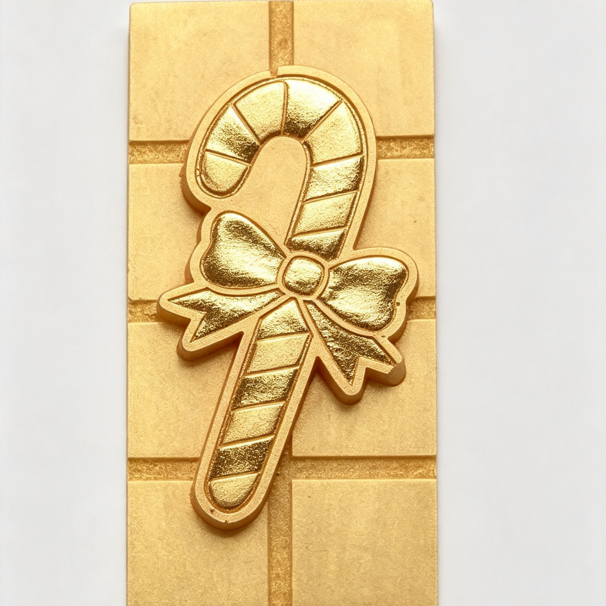 A gold-colored candy caneCandy Cane Mini Snap Barrectangular plaque featuring a gift box design, set against a plain light gray background.