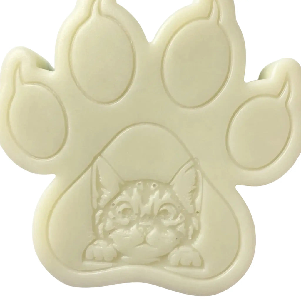 An off-white paw-shaped WAX MELT featuring an embossed kitten face in the center, shown against a plain white background.