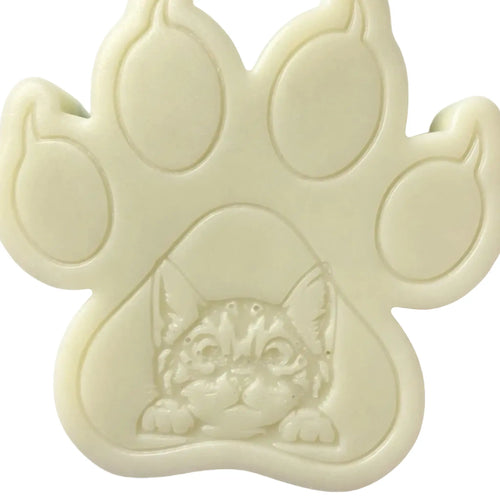 An off-white paw-shaped WAX MELT featuring an embossed kitten face in the center, shown against a plain white background.