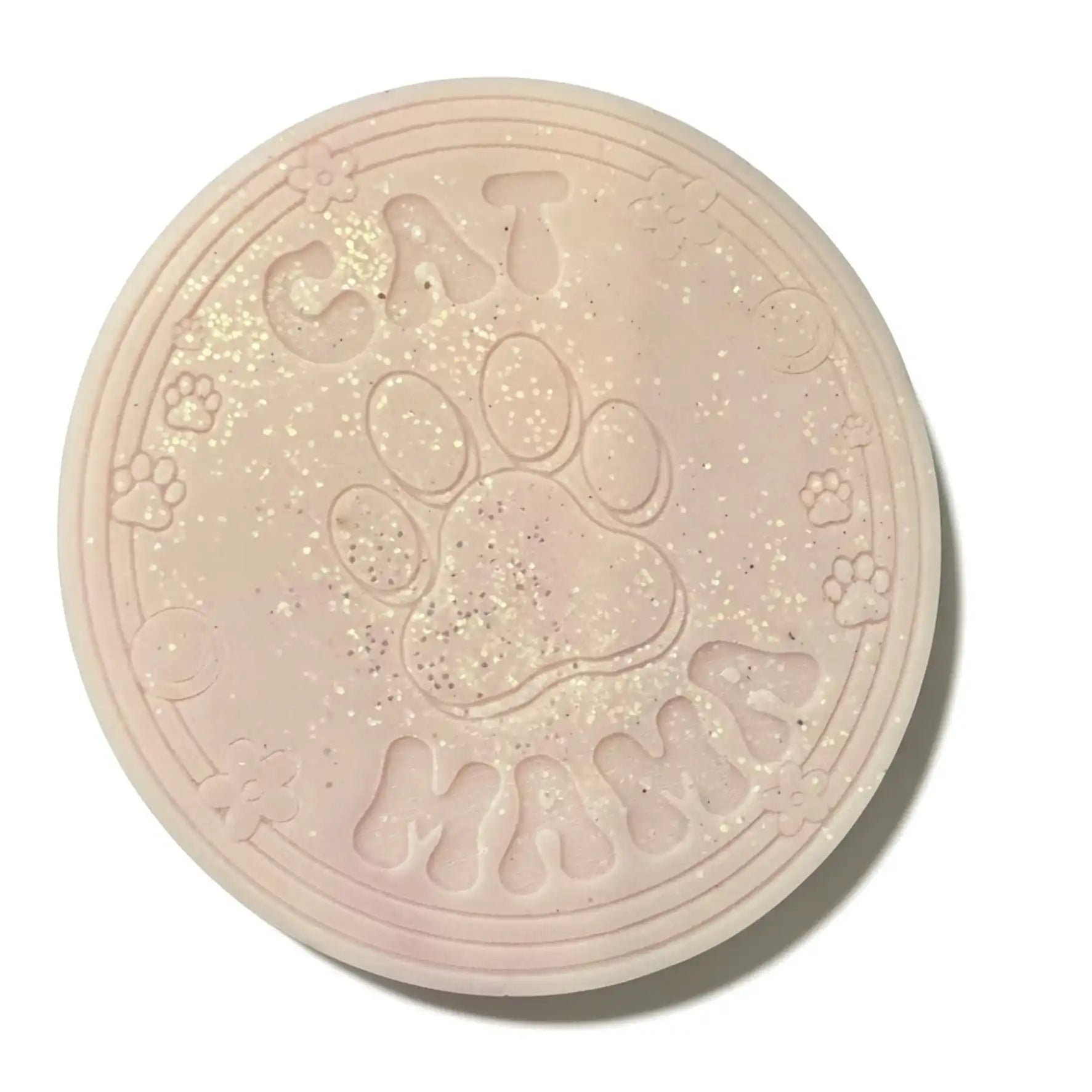 A round, pale pink novelty item with embossed text reading 'CAT MAMA EAX MELT ' and a large paw print in the center, decorated with fine glitter, shown on a white background.