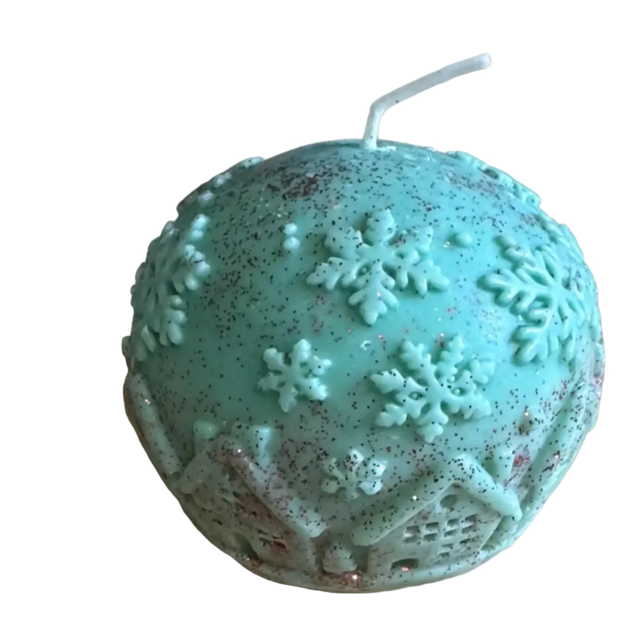 A round teal green candle with embossed snowflakes and house motifs, decorated with dark red glitter specks, sitting on a wooden cutting board.