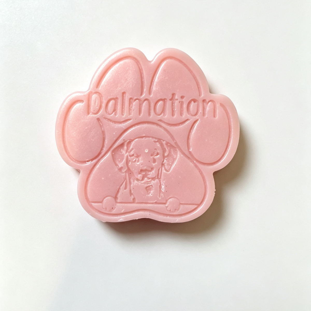 A pink paw-shaped wax melt embossed with the word 'Dalmation' and a Dalmatian dog face, photographed on a plain white background.