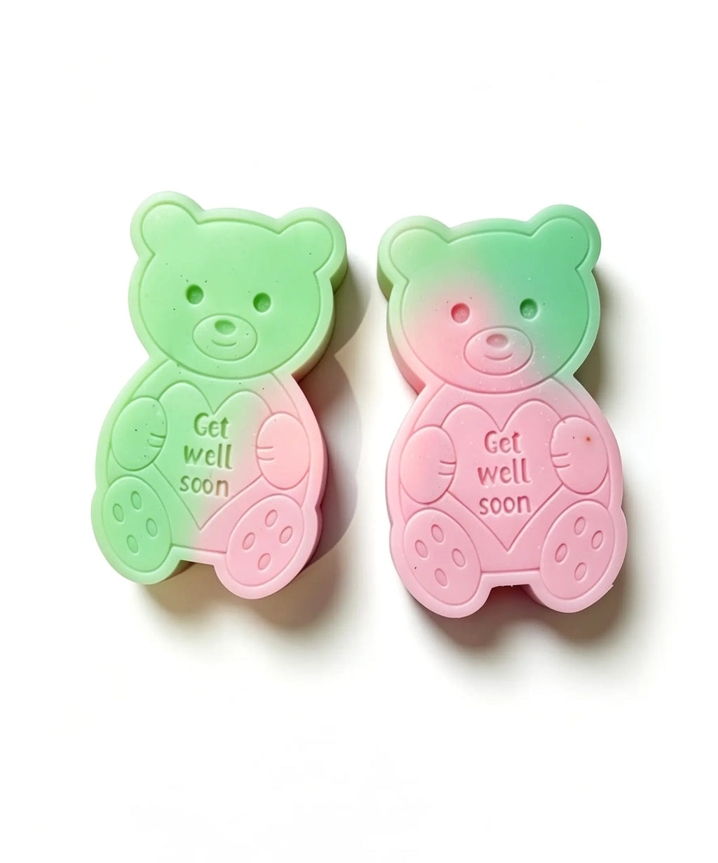 Two teddy bear-shaped WAX MELT  on a white background, one with a green-to-pink gradient and the other with a pink-to-green gradient, both featuring the text 'Get well soon' on the front.