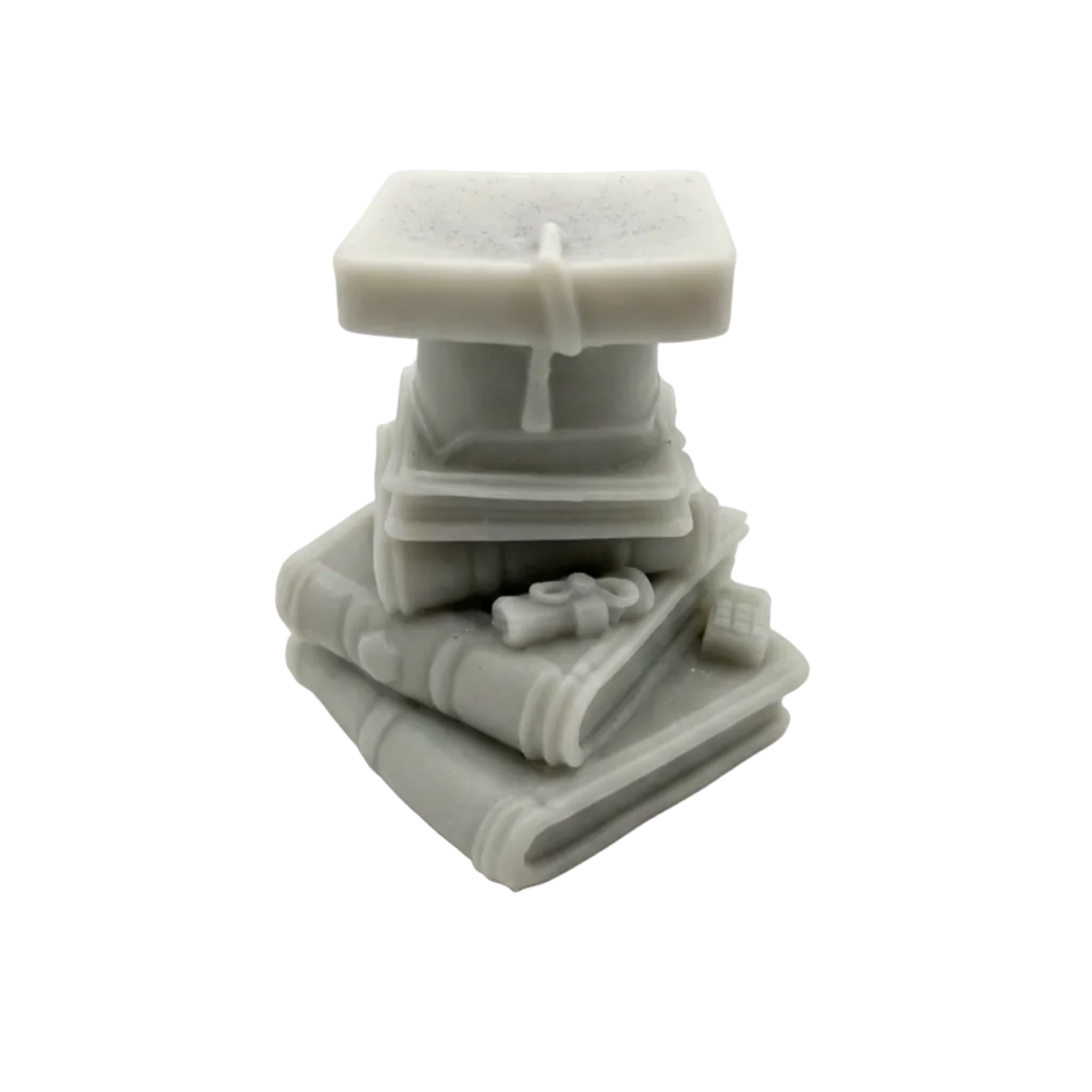 A small gray sculptural Wax Candle  figurine depicting a stack of books with a graduation cap and tassel, photographed on a seamless white background.