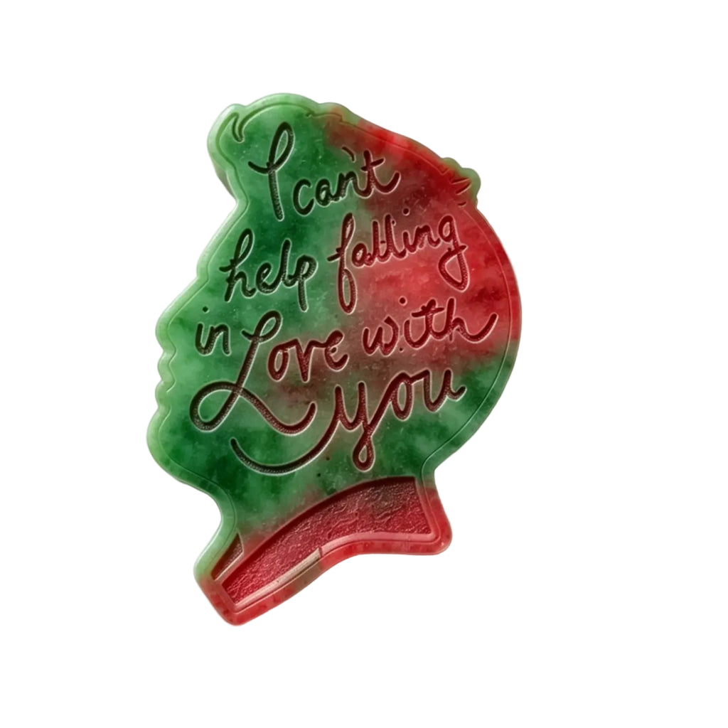 A-wax melt  like a silhouette of a woman's profile, featuring a green and red watercolor gradient background with the cursive text 'I can't help falling in love with you' in dark red-brown lettering, shown on a plain white background.