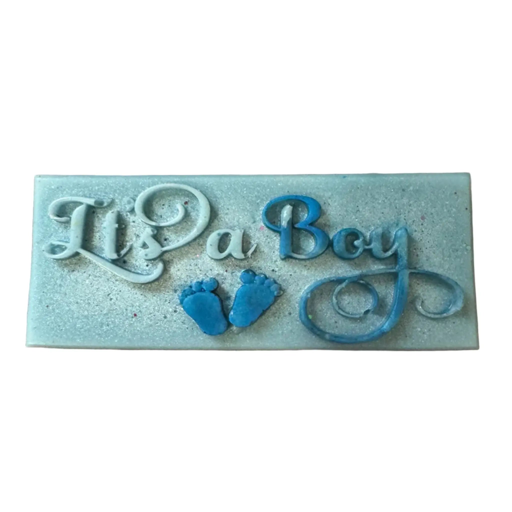 A rectangular light blue decorative plaque with embossed text reading 'It's a Boy' in white and blue, plus two small blue baby footprints, shown on a plain white background. wax melt