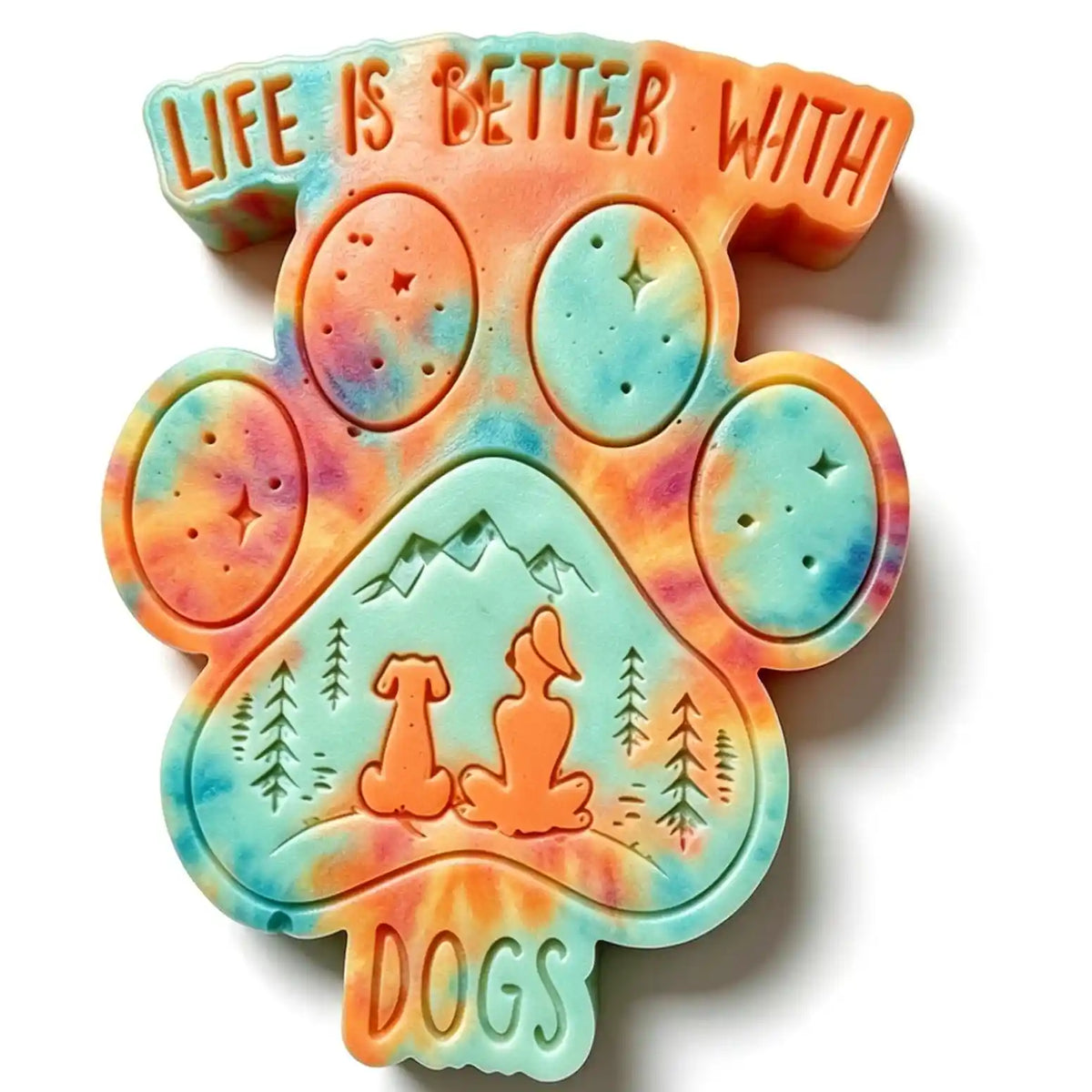 A colorful tie-dye dog-shaped soap or plaque featuring the text 'LIFE IS BETTER WITH DOGS' and an embossed mountain-and-dog landscape, shown on a plain white background. WAX MELT