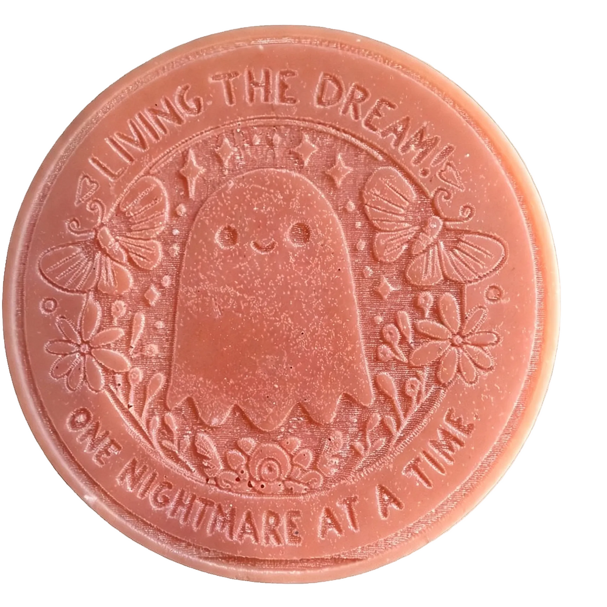 A round peach-colored wax melt featuring a cute ghost design with butterflies and flowers, embossed with the text 'Living The Nightmare Wax Melt