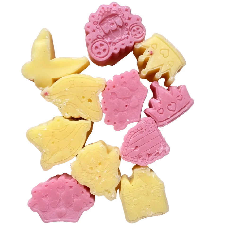 A group of small, molded WAX MELTS in pastel yellow and pink, featuring whimsical shapes like a butterfly, a leaf, a crown, a castle, and a flower, arranged on a plain white background.