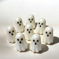 Seven small white ghost-shaped figurines with black eyes and mouths, arranged on a light beige surface with soft shadows. Marshmallow Ghost Wax melts 
