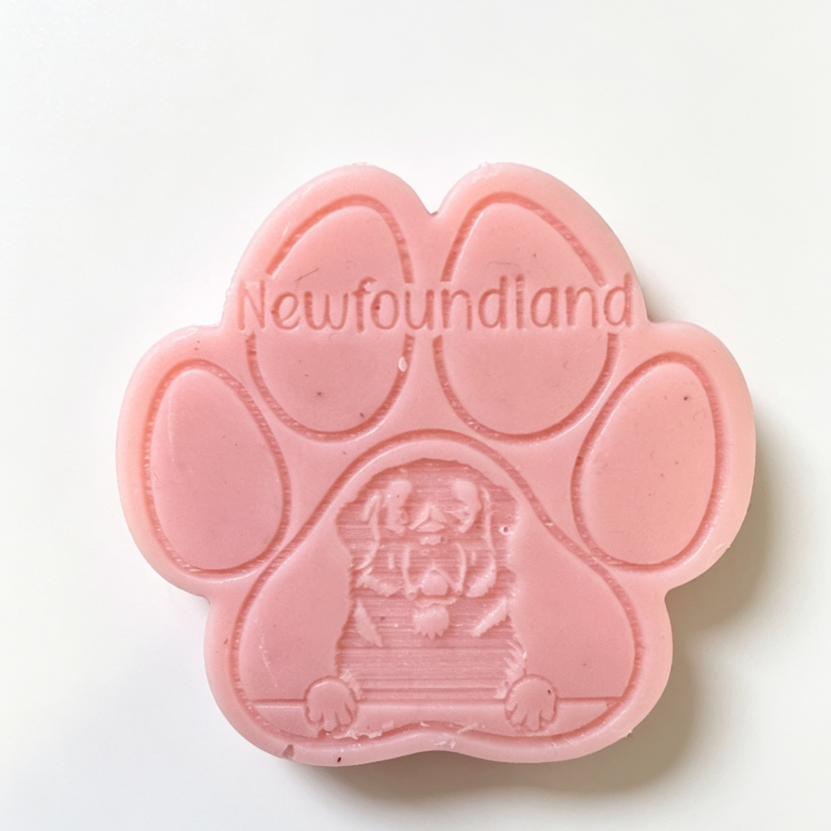 A pink paw-shaped wax melt embossed with the word 'Newfoundland' and a Newfoundland dog illustration, photographed on a plain white background.
