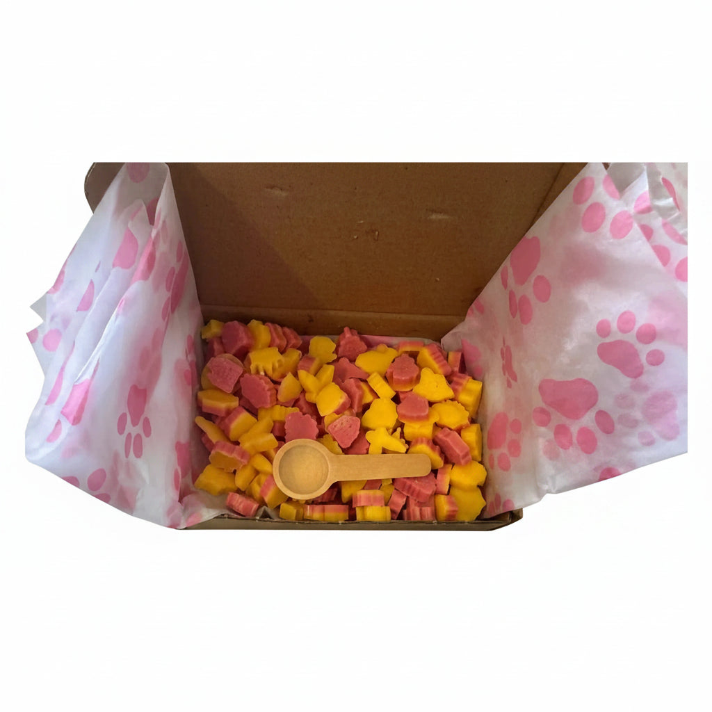 An open cardboard box lined with pink paw-print tissue paper, filled with small yellow and pink dog treats and a small wooden scoop. scopes wax melts