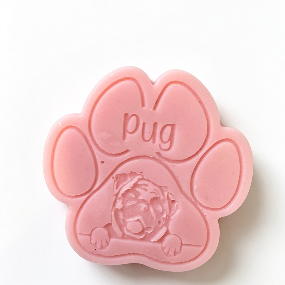 A pink paw-shaped wax melt featuring an embossed pug dog face and the word 'pug' molded into one of the paw pads, set against a plain white background.