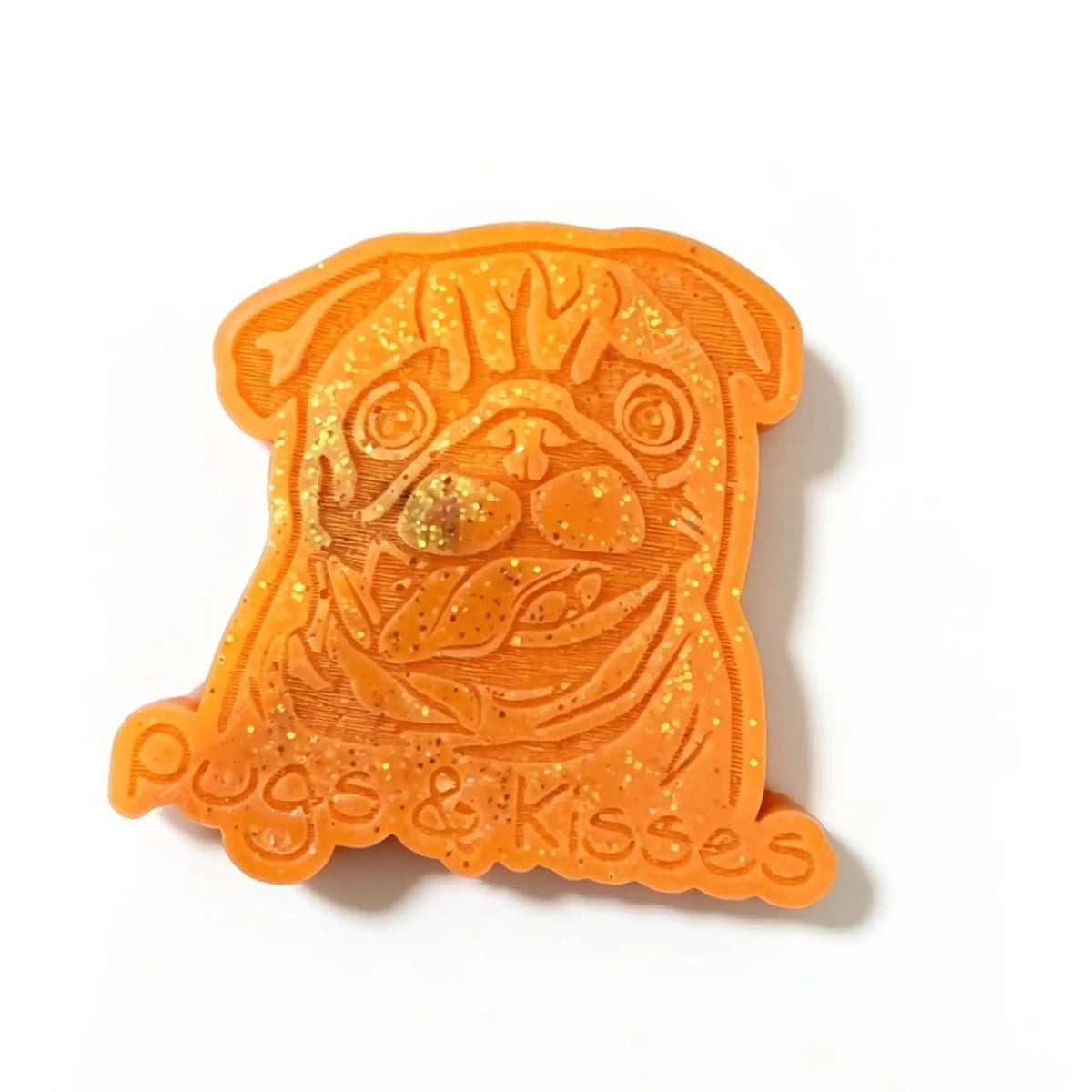 An orange 3D-printed pug-shaped sticker or charm with glittery orange wax melt and the text 'Pugs & Kisses' at the bottom, shown on a plain white background.