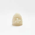 A hand holding a small,wax melt, cream-colored silicone or rubber accessory with a raised bee design, set against a plain white background.