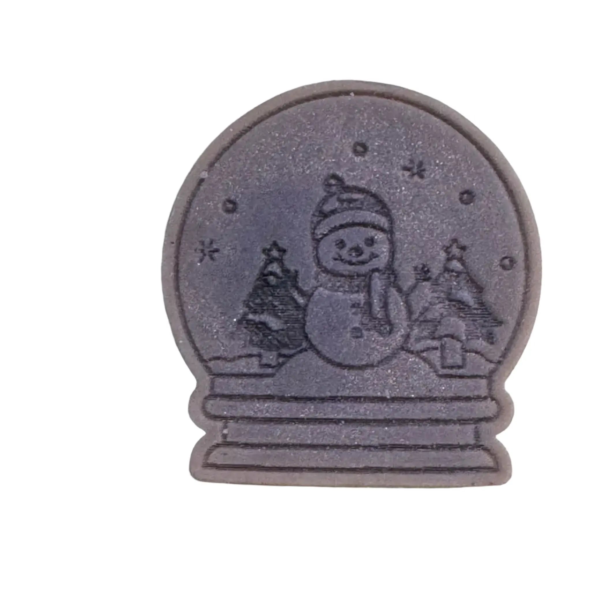 A round, dark gray decorative item featuring an embossed snowman wearing a hat and scarf, with small trees and stars inside a globe-like border, shown on a plain white background. wax melt