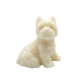 A small sculpted CANDLE of a seated dog, likely made of soap or resin, in a warm off-white or cream color, set against a plain white background.