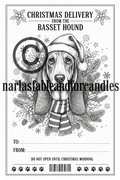 A black and white Christmas-themed delivery card or envelope design featuring an illustration of a basset hound wearing a Santa hat and striped scarf, surrounded by holiday foliage and snowflakes. Text reads 'Christmas Delivery from the Basset Hound' with blank 'To:' and 'From:' fields and a barcode at the bottom.