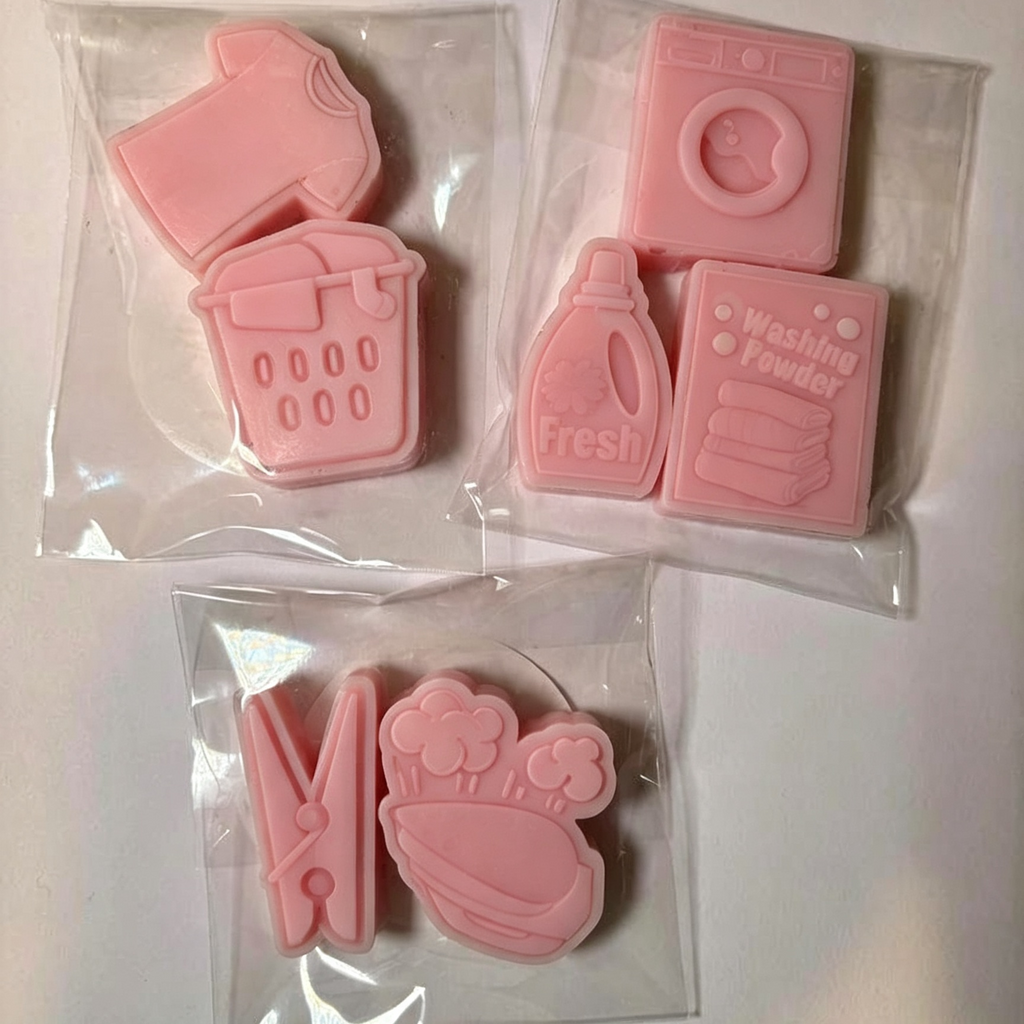 Four pink laundry-themed wax melts in clear plastic bags, including a clothes dryer, washing machine, detergent bottle, washing powder box, clothes clip, and bathtub with steam.