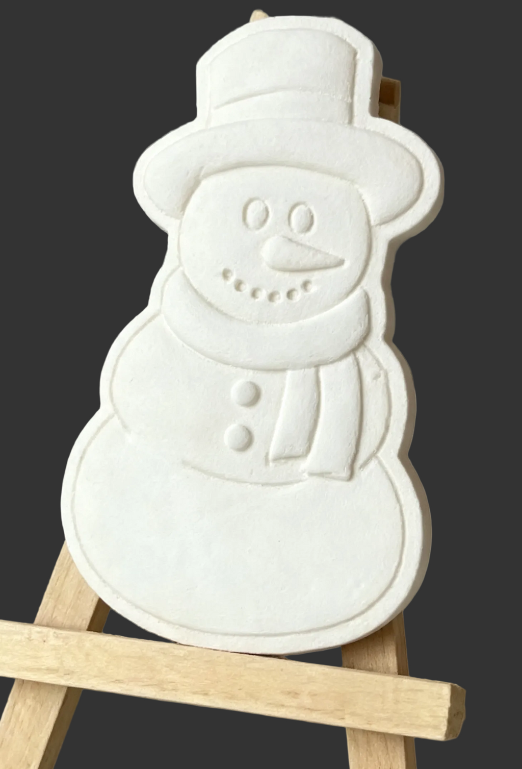 A white snowman-shaped plaque ecorative or cookiewax melt wooden easel against a neutral gray background.