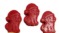 Three red dog-shaped wax melts wearing Santa hats arranged on a light wood grain surface.